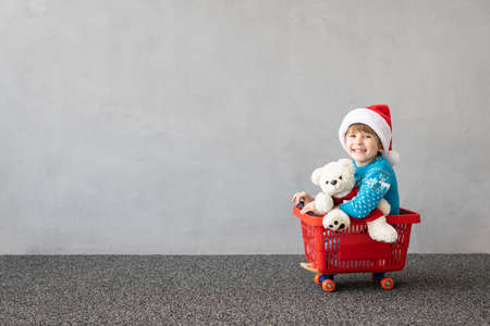 Happy child wearing Christmas costume. Kid riding shopping cart. Funny child playing. Kid having fun outdoor in winter. Xmas sale conceptの写真素材