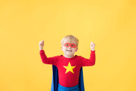 Portrait of superhero child. Super hero kid against yellow paper background. Happy child wearing red mask and cape of superhero. Children dream and imagination conceptの写真素材