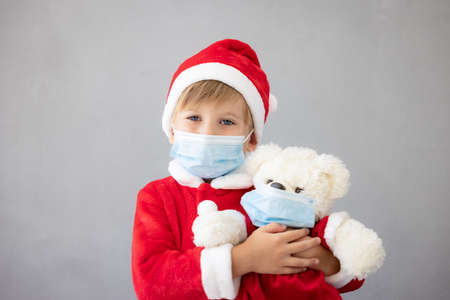 Portrait of child wearing medical mask. Kid holding teddy bear. Christmas holiday during coronavirus covid-19 pandemic conceptの写真素材