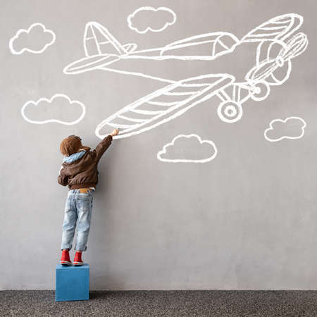 Dream big! Happy kid draws a chalk airplane on the wall. Children imagination and travel conceptの写真素材