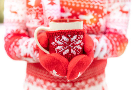 Girl holding the cup of mulled wine in hands outdoor in winter. Female wearing sweater and gloves with Christmas ornament. Xmas holiday conceptの写真素材