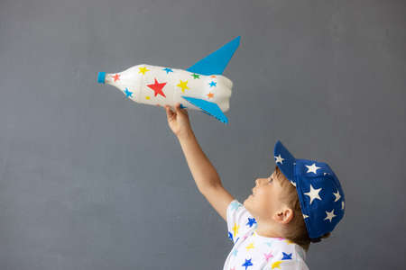 Happy child playing with toy rocket against concrete wall background. Kid pretend to be astronaut. Imagination and children dream conceptの写真素材
