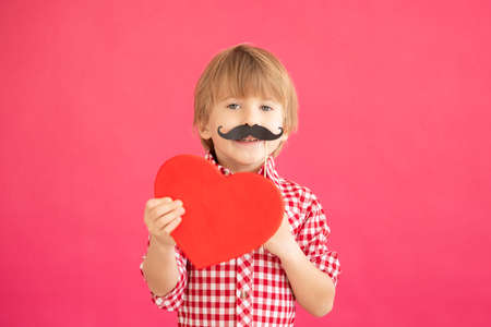Happy child holding heart in hands. Portrait of smiling kid against pink background. Valentines day holiday conceptの写真素材