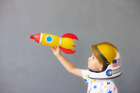 Happy child playing with toy rocket against concrete wall background. Kid pretend to be astronaut. Imagination and children dream conceptの写真素材