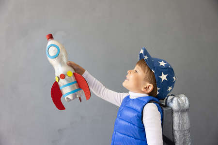 Happy child playing with toy rocket against concrete wall background. Kid pretend to be astronaut. Imagination and children dream conceptの写真素材