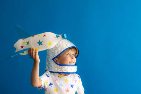 Happy child playing with toy rocket against blue background. Kid pretend to be astronaut. Imagination and children dream conceptの写真素材