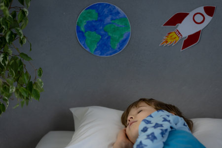 Happy child sleeping with toy rocket and teddy bear. Kid pretend to be astronaut. Imagination and...