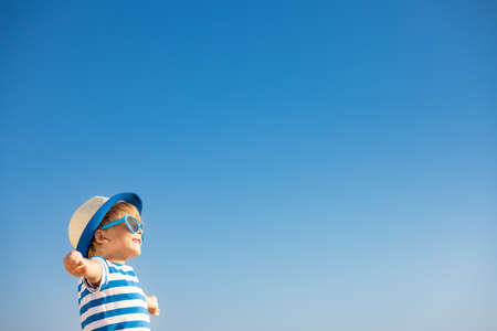 Happy child having fun outdoor against blue sky background. Portrait of smiling kid on summer vacation. Freedom and travel conceptの写真素材