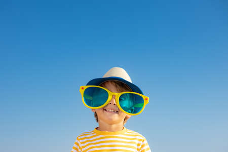 Happy child having fun outdoor against blue sky background. Portrait of smiling kid on summer vacation. Freedom and travel conceptの写真素材