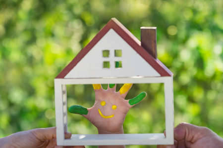 Happy child with smile on hand. Family holding house in hands against spring green background. Real estate and ecology conceptの写真素材