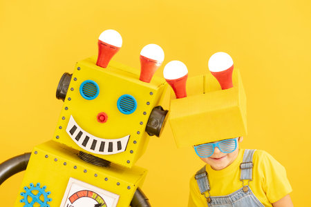 Happy child with robot against yellow background. Funny kid playing at home. Success, creative and...