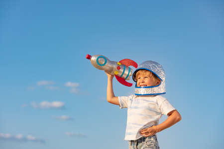 Happy child playing outdoor with toy rocket against blue summer sky background. Kid pretend to be astronaut. Imagination and children dream conceptの写真素材
