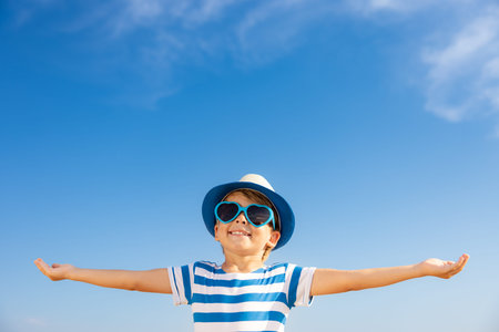 Happy child having fun outdoor against blue sky background. Portrait of smiling kid on summer...