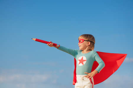 Superhero child playing outdoor. Super hero kid against blue summer sky background. Imagination and freedom conceptの写真素材