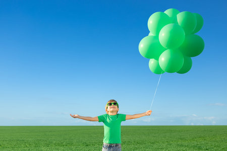 Happy child playing with bright multicolor balloons outdoor. Kid having fun in green spring field...