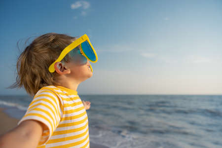 Happy child enjoying the sun against blue sky background. Kid having fun on the beach. Summer vacation and holiday conceptの写真素材
