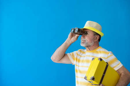 Happy senior man ready to travel. Person looking through binoculars. Summer vacation and holiday conceptの写真素材