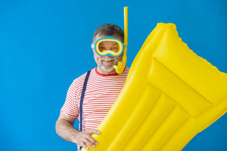 Happy senior man ready to travel. Person holding yellow air mattress. Summer vacation and holiday conceptの写真素材