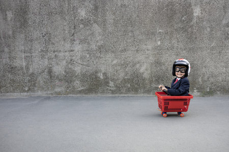 Happy child pretend to be businessman. Funny kid riding shopping cart outdoor. Back to work, start up and business idea conceptの写真素材