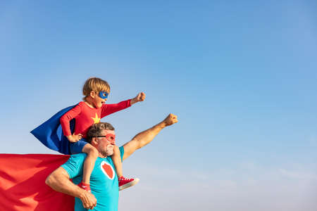 Superhero senior man and child playing outdoor. Super hero grandfather and boy having fun together against blue summer sky background. Family holiday concept. Happy Father's dayの写真素材