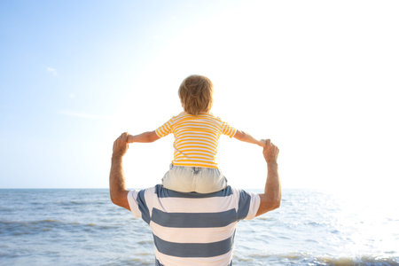 Happy family having fun on the beach. Father and son against blue sea and sky background. Summer vacation and fathers day concept. Rear view portraitの写真素材