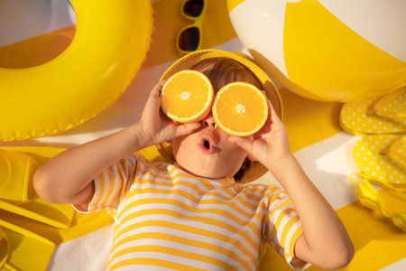 Surprized child holding slices of orange fruit like sunglasses. Kid wearing striped yellow t-shirt...