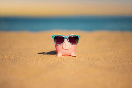 Piggybank on the beach against sea and sky background. Savings for summer travel and vacation conceptの写真素材