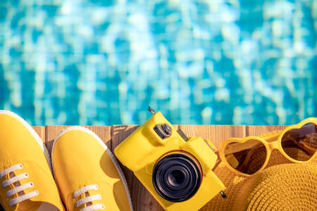 Yellow sneakers and camera on blue wood against water background. Summer vacation and travel concept conceptの写真素材