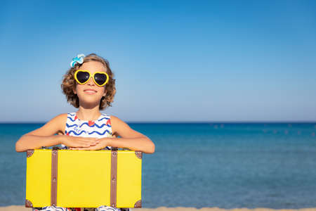 Child with vintage suitcase on summer vacation. Girl having fun on the beach. Kid sitting against sea and sky background.  Travel and adventure conceptの写真素材