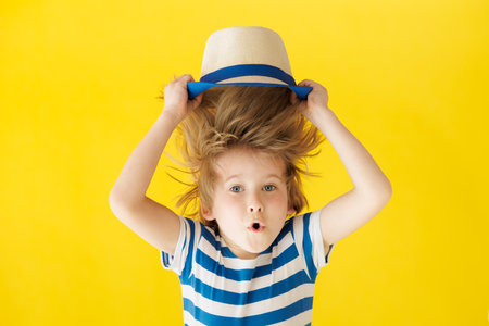 Surprised child holding face. Shocked kid against yellow background. Boy wearing striped shirt. Summer vacation and travel conceptの写真素材