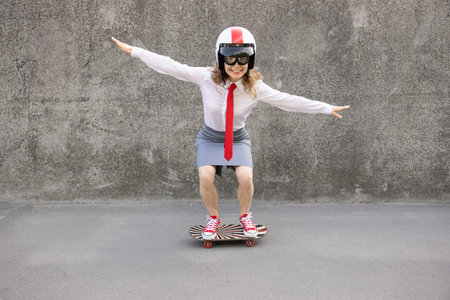Happy businesswoman riding skateboard. Outdoor portrait of young woman. Back to work, start up and business idea conceptの写真素材