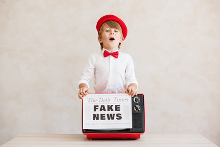 Newsboy shouting against grunge wall background. Boy selling fake news. Child wearing vintage costume. Kid holding newspaper. Social media and Internet nerwork conceptの写真素材