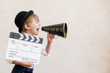 Newsboy shouting through loudspeaker against grunge wall background. Boy selling fake news. Child...