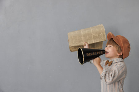 Newsboy shouting through loudspeaker against grunge wall background. Kid selling newspaper. Child...