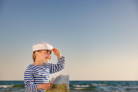 Happy child pretend to be sailor. Kid agains blue sea and sky. Boy on summer vacation. child holding map. Adventure and travel conceptの写真素材