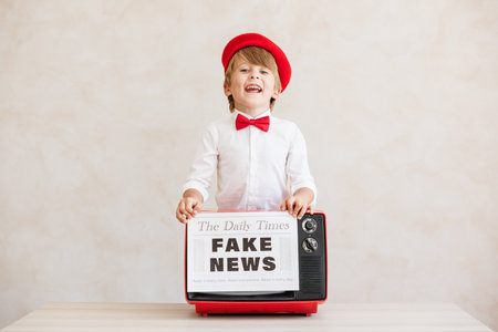 Newsboy shouting against grunge wall background. Boy selling fake news. Child wearing vintage costume. Kid holding newspaper. Social media and Internet nerve work conceptの写真素材