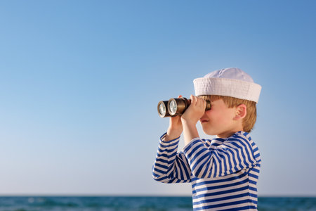 Happy child pretend to be sailor. Kid agains blue sea and sky. Boy on summer vacation. Child looking through binoculars. Adventure and travel conceptの写真素材