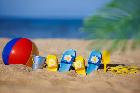 Kids flip-flops, beach ball and snorkel on yellow sand against blue sea background. summer vacation conceptの写真素材
