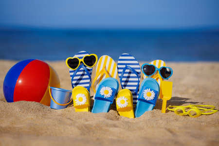 Family flip-flops, beach ball and snorkel on yellow sand against blue sea background. Summer vacation and travel conceptの写真素材