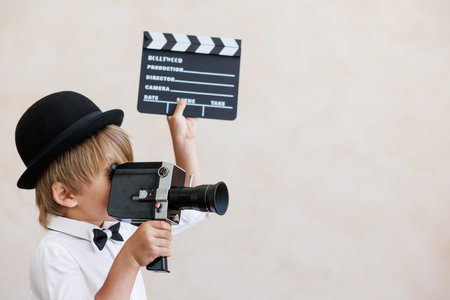 Director shouting against grunge wall background. boy playing at home. Child wearing vintage costume. Kid holding camera and clapper. Social media and Internet nerve work conceptの写真素材