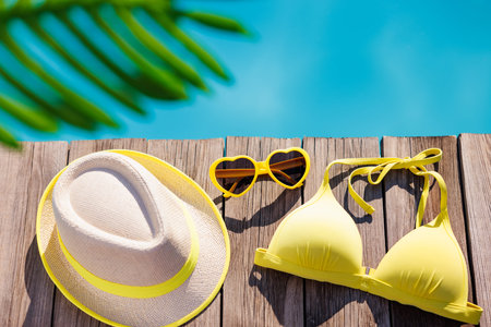 Beach swimsuit and sunglasses on wooden background. Things for vacation against blue water of...