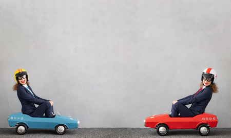 Successfull businesswomen driving toy car outdoor. Funny young woman against concrete wall...