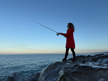 A young happy woman is fishing at sea against blue sky background. Girl having fun during spring vacationの写真素材
