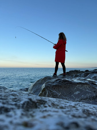 A young happy woman is fishing at sea against blue sky background. Girl having fun during vacationの写真素材