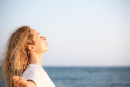 Young happy woman enjoying by sunrise against blue sky background. Female walking along the beach on summer vacationの写真素材
