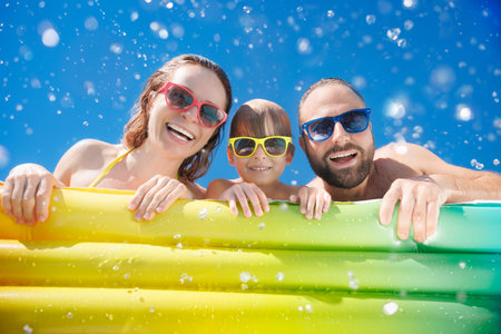 Happy family playing in waterpark. People having fun on summer vacation. Family jumping into swimming pool with splashes of water.の写真素材