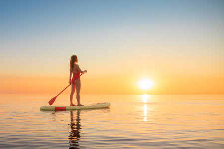 Young woman walking on stand up paddle sup boards by the sea during summer vacation. Beautiful girl...