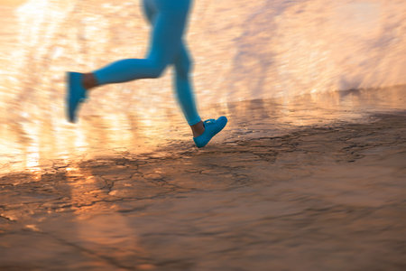Motion blurred legs of fit woman against sea background; workout and cardio. Wellness, exercise and...