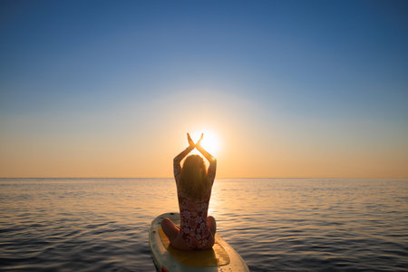 Happy woman walking on stand-up paddleboard by the sea. Female enjoying by sunrise during summer...