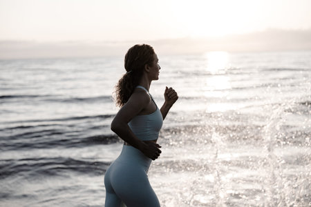 Sporty young woman is running against sea background during her vacation. Female doing workout and...